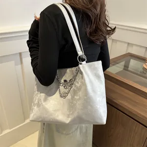 Detail of silver metallic tote bag with black bow pendant and pleated texture shoulder bag