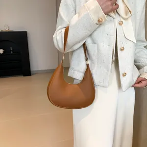 Close-up of minimalist brown crescent shoulder bag with matte leather and gold hardware