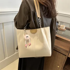 Detail of cream tote bag with Fashion tag, metal chain strap and pink plush monster charm