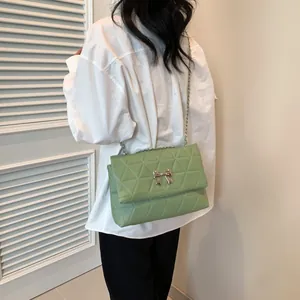 Side view of a mint green quilted crossbody bag with a silver bow clasp on a model