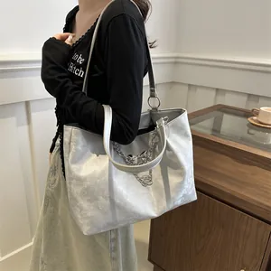 Detail of silver metallic tote bag with decorative chain and bow pendant charm