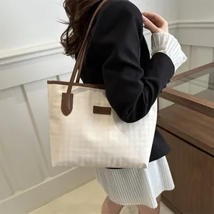 Detail of a chic cream and houndstooth tote bag with brown straps worn by a model