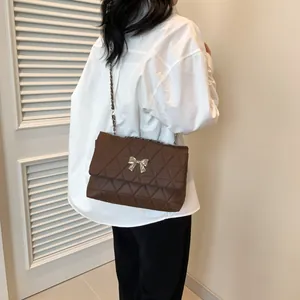 Detail of a brown quilted crossbody bag with a silver bow clasp shown on a model