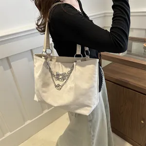 Detail of a large cream hobo bag with silver chain and bow pendant on a female model