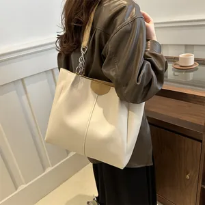 Beige pleated tote bag with chain strap shown from a side view on a model in a room
