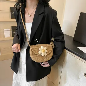 Detail of hand-woven straw crossbody bag with white daisy flower and slim shoulder strap