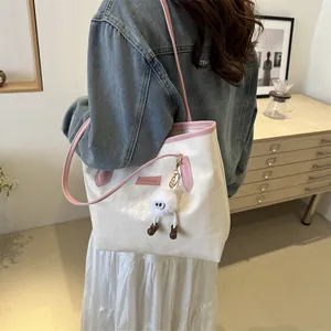 Lifestyle view of a cream and pink tote bag with a cute plush charm on a model