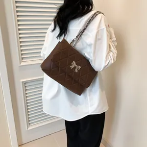 Detail of a dark brown quilted shoulder bag with a silver bow buckle on a model
