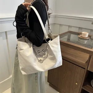 Detail of off-white tote bag featuring silver chain straps with bow and heart pendants