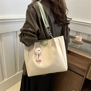Detail of off-white tote bag with green trim, Fashion logo, and pink plush charm
