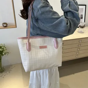 Close-up of a cream woven tote bag with pink leather trim and brand label detail