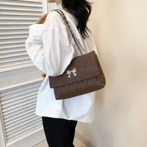 Dark brown quilted shoulder bag with silver bow detail worn by model on shoulder