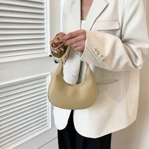 Chic beige crescent shoulder bag with smooth matte finish shown on a model