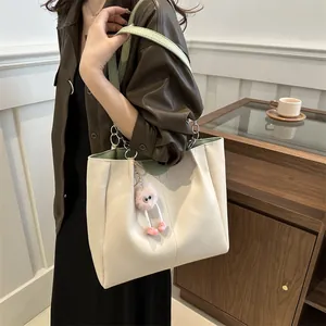 Lifestyle view of large beige and green tote bag with pink plush keychain on shoulder