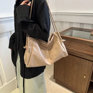 Close-up of beige faux leather tote with embossed lettering and side knot drawstring
