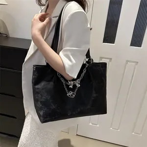 Detail of black tote bag with silver metal chains and bow pendant on a white suit
