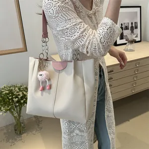 Detail of cream white tote bag featuring pink chain strap and cute plush monster charm