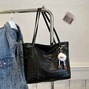 Detail of black houndstooth embossed tote bag with plush charm and fashion metal plate