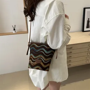 Side view of checkered knit bucket bag with brown leather strap and fashion patch