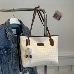 Detail of houndstooth tote bag featuring leather handles and a cute plush monster charm
