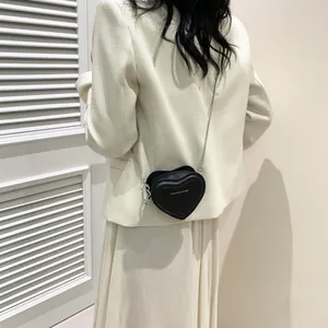 Vue arrière du sac cœur noir à chaîne argentée porté sur une veste de blazer beige