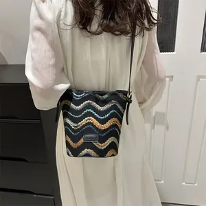 Knitted wave pattern bucket bag in black and teal, styled with a white dress on a model