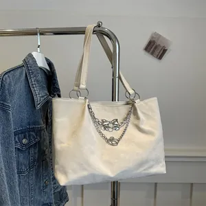 Detailed view of cream tote bag featuring silver chain decor and elegant metal bow pendant
