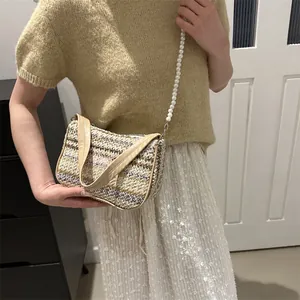 Detail of woven straw bag featuring butterfly accent and elegant faux pearl shoulder strap