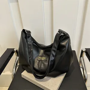 Detailed close-up of a black matte leather shoulder bag with a gold fashion logo emblem