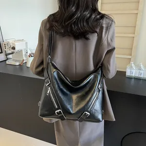 Close-up of black glossy leather tote bag showing silver zipper details and adjustable straps