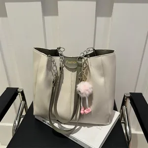 Detail of a chic cream tote bag with olive trim and plush doll charm on a chair