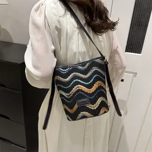 Detail of canvas bucket bag featuring colorful wave embroidery and a leather fashion tag