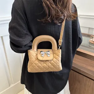 Close-up of khaki quilted handbag featuring silver bow hardware on black pleated dress