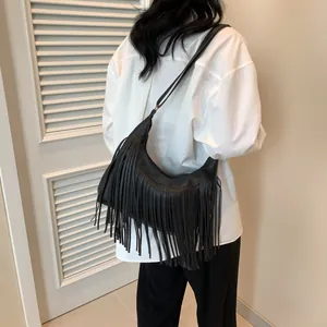 Vue détaillée des longues franges sur un sac hobo en cuir noir porté par un mannequin