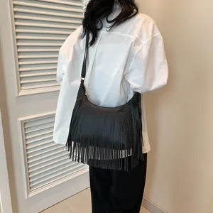 Détail du sac hobo noir avec de longues franges et texture cuir litchi porté par un modèle