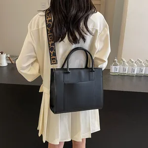 Sac fourre-tout noir avec large bandoulière décorative porté par un mannequin de dos