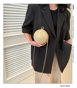 Detail einer beigen geflochtenen Kugel-Abendtasche mit Goldkette, getragen zu einem schwarzen Anzug