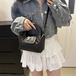 Close-up of black quilted crossbody bag with silver bow hardware worn by a model