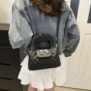 Close-up of black quilted shoulder bag with silver bow buckle on model with denim jacket