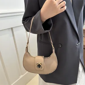Detail of beige crescent hobo bag featuring a gold clover metal clasp on a black blazer
