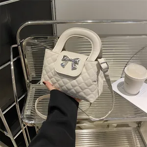Close-up of a white quilted tote bag featuring a silver bow-knot metal hardware detail