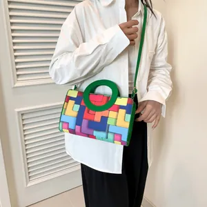 Detail view of a colorful block pattern handbag with a green round handle on a model
