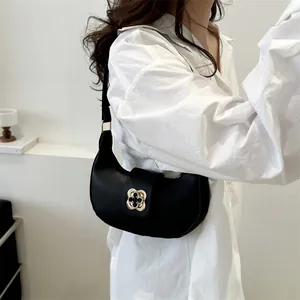Detail shot of black crescent shoulder bag with golden clover-shaped metal clasp