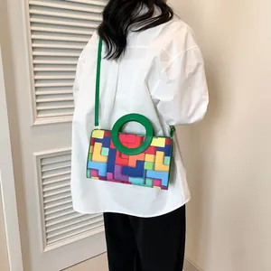 Detail of colorful geometric block pattern and green round handle on a crossbody bag