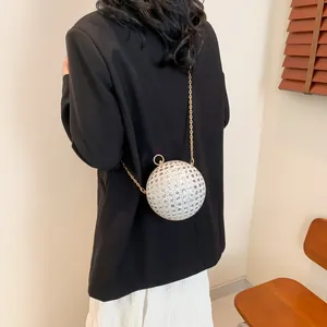 Detailaufnahme einer silbernen Kugel-Abendtasche mit goldener Kette am Outfit