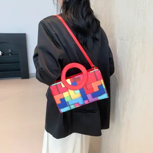 Detail view of colorful geometric crossbody bag with red circular handle and leather strap
