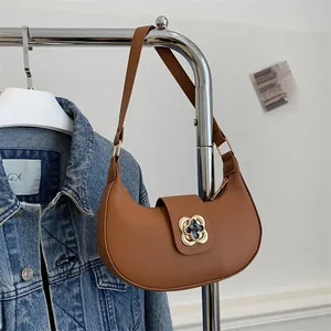 Detail of a brown crescent shoulder bag with a gold clover clasp on a denim jacket background