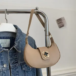 Detail of beige crescent shoulder bag with golden clover buckle on a clothing rack