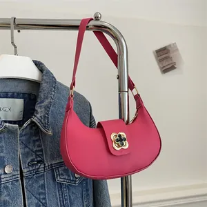 Detail of rose red crescent shoulder bag with golden clover metal clasp and leather texture