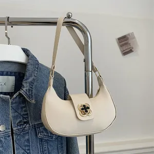 Detail of cream hobo bag with vintage gold flower buckle hanging on a metal rack